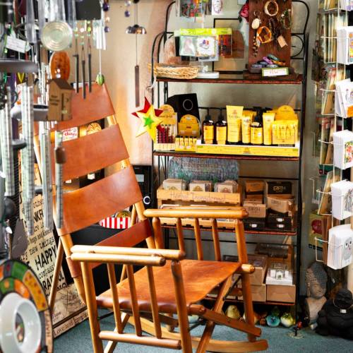 A cozy shop corner featuring a wooden rocking chair, shelves of colorful products, and various decorative items.