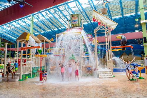 A vibrant indoor water park with a large water slide and kids playing under a waterfall feature.