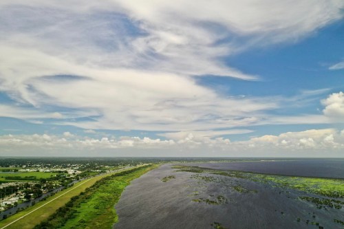 Aerial view of a wide waterway bordered by green land and a blue sky with scattered clouds.