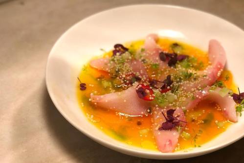 A white bowl filled with colorful fish slices, garnished with herbs and edible flowers in a vibrant sauce.