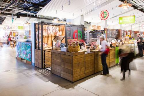 A bustling market stall with wooden decor, showcasing various products and people shopping in a vibrant space.