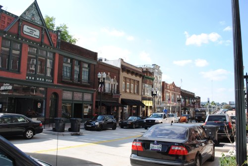 A bustling street lined with historic buildings and parked cars under a clear blue sky.