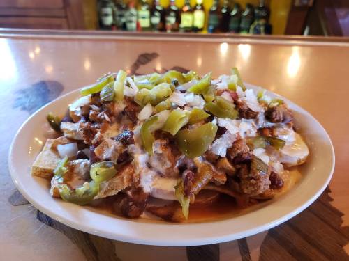 A plate of nachos topped with meat, cheese, onions, and green peppers, served on a wooden table.