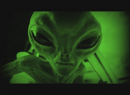 A close-up of a green-tinted alien figure with large eyes and a serious expression.