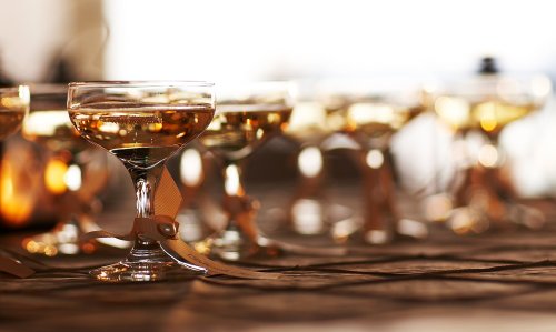 A row of elegant champagne glasses filled with sparkling drinks, set on a wooden table with soft lighting.