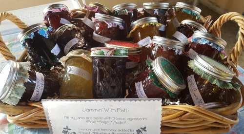 A basket filled with various jars of homemade jams, labeled with flavors, alongside a sign about the ingredients used.