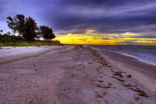 A serene beach at sunset, with gentle waves, sandy shore, and dark clouds contrasting the vibrant sky.