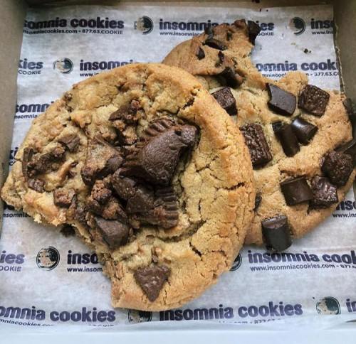Two large cookies in a box, one with chocolate chunks and the other with chocolate pieces and chunks.