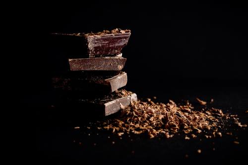 A stack of dark chocolate bars with chocolate shavings scattered on a black background.