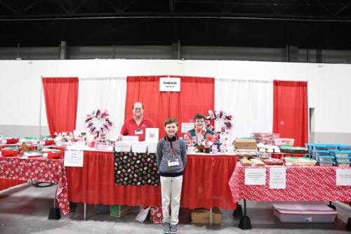 A festive booth with red and white decor, featuring three people and various baked goods on display.