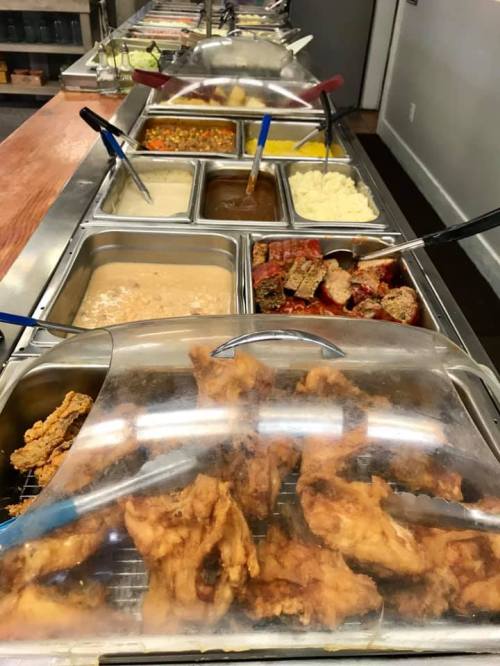 A buffet line featuring various dishes, including fried chicken, meatloaf, mashed potatoes, and assorted sides.