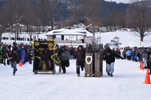 Participants race with homemade sleds in a snowy landscape, surrounded by a cheering crowd.