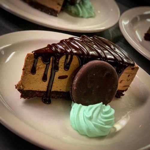 A slice of chocolate mousse cake topped with chocolate drizzle, a mint swirl, and a chocolate cookie on a white plate.