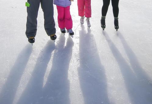 Four pairs of ice skates on a frozen surface, casting long shadows in the sunlight.
