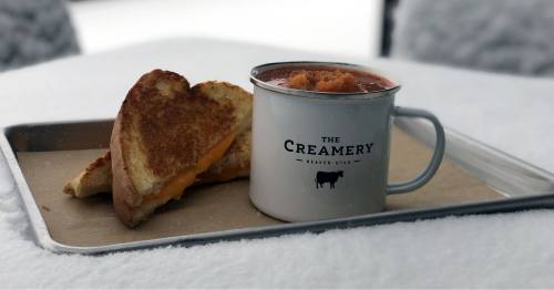 A grilled cheese sandwich on a tray next to a mug of hot chocolate, set on a snowy surface.