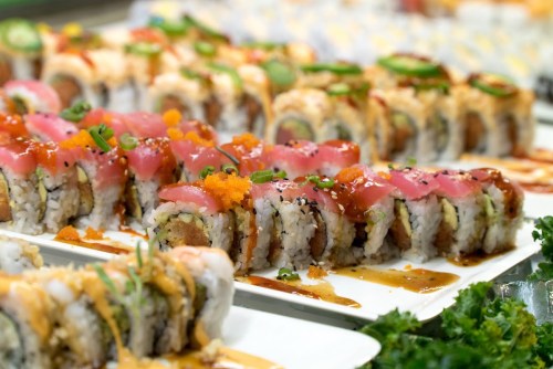 A colorful assortment of sushi rolls, featuring tuna, avocado, and various toppings, arranged on white plates.