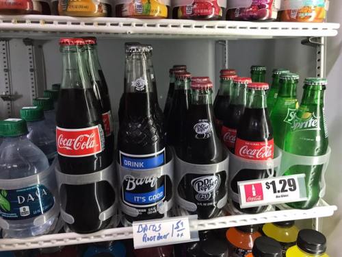 A vending machine shelf displaying various soda bottles, including Coca-Cola, Barq's, Dr Pepper, and Sprite.
