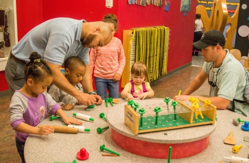 Adults and children engage in a hands-on activity with colorful building materials at a playful learning space.