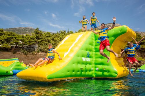 A group of children in life jackets play on a colorful inflatable water slide, jumping into the water on a sunny day.