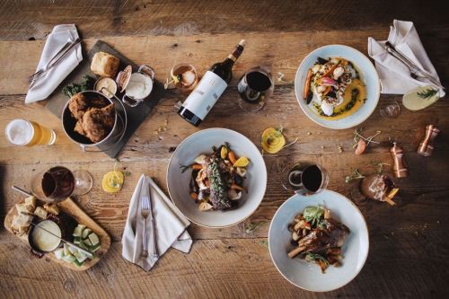 A beautifully arranged table with various gourmet dishes, drinks, and bread on a rustic wooden surface.