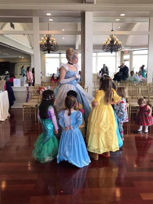 A princess in a blue gown interacts with a group of children in colorful costumes at a festive event.