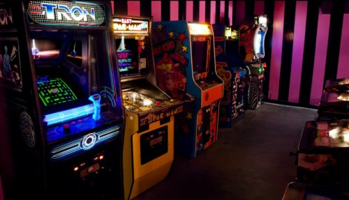 A row of vintage arcade machines in a dimly lit room with purple striped walls.