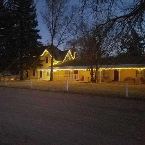 A yellow house decorated with string lights, surrounded by trees, at dusk with a clear sky.