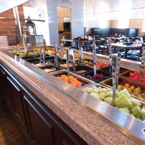 A buffet station with various fresh fruits and toppings in containers, set in a restaurant dining area.