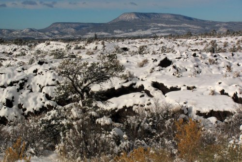 Snow-covered landscape with rocky terrain and distant mountains under a clear blue sky.