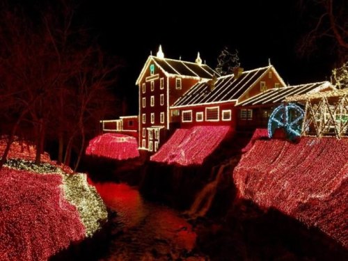 A beautifully lit building surrounded by vibrant holiday lights, reflecting on a nearby stream at night.