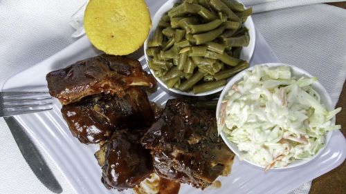 A plate featuring barbecue ribs, green beans, coleslaw, and a cornbread muffin.