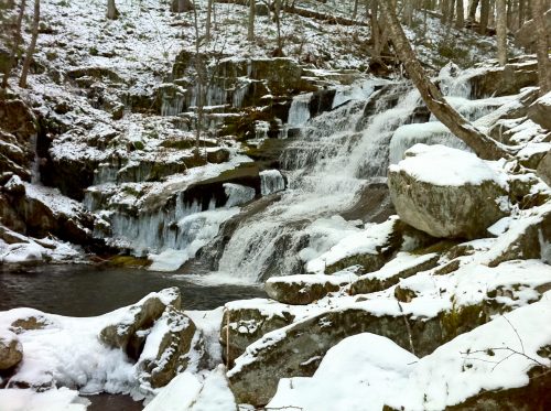 A serene waterfall cascades over rocky terrain, surrounded by snow-covered trees and a tranquil pool below.