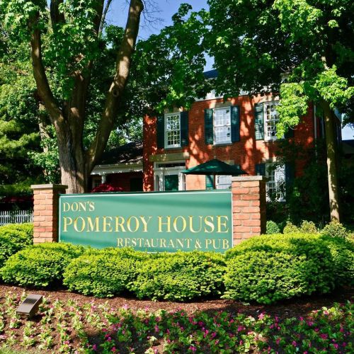 Sign for Don's Pomeroy House Restaurant & Pub in front of a brick building surrounded by greenery and flowers.