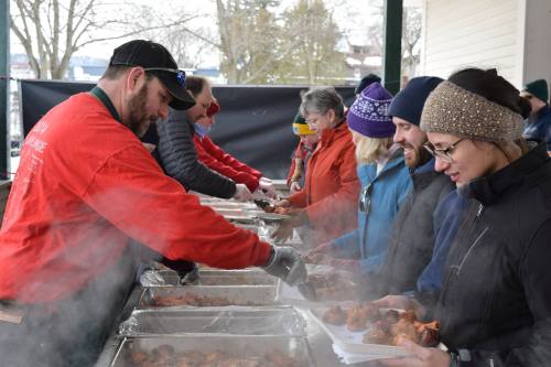 A group of people enjoying a food event, serving and receiving steaming dishes outdoors in winter attire.