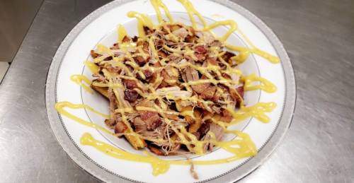 A plate of shredded meat topped with crispy bits and drizzled with yellow mustard.