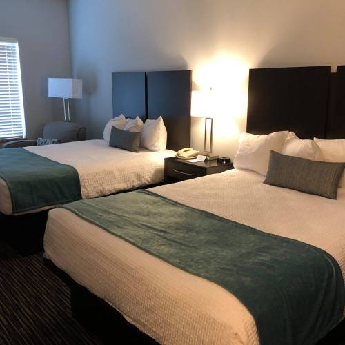 A hotel room with two beds, a sofa, and a lamp, featuring light-colored bedding and teal accents.