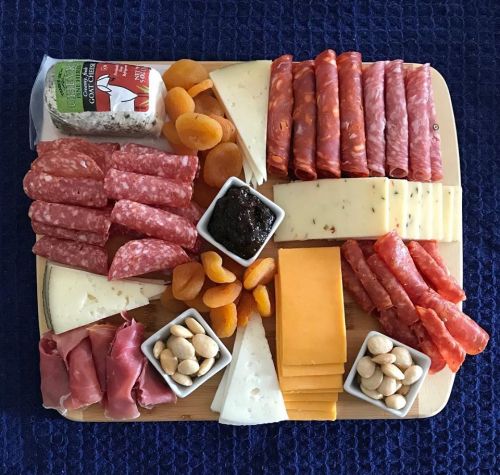 A wooden platter arranged with various meats, cheeses, dried fruits, and nuts, creating a colorful charcuterie display.