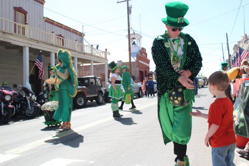 A child in a red shirt reaches out to a person in a green costume during a festive parade celebration.