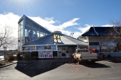 A McDonald's restaurant with a unique glass design, featuring a sign for $1 soft drinks. A vintage truck is parked outside.