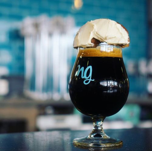 A glass of dark beer topped with a slice of apple and cream, set against a blue background.