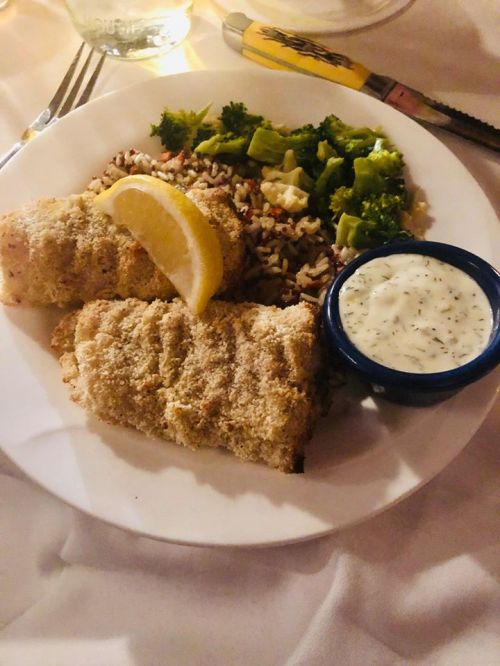 A plate with two breaded fish fillets, a lemon wedge, rice, broccoli, and a small bowl of dipping sauce.
