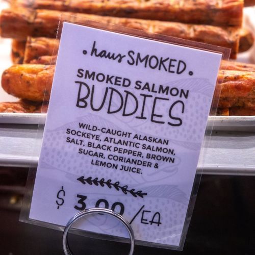 Sign for smoked salmon buddies, listing ingredients: wild-caught salmon, salt, pepper, brown sugar, coriander, lemon juice. $3.00 each.