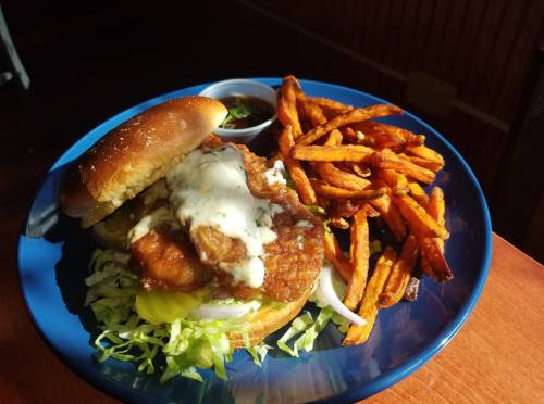 A crispy fried chicken sandwich with lettuce, pickles, and sauce, served with sweet potato fries on a blue plate.