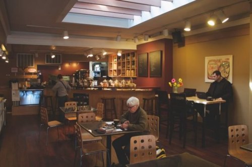 A cozy café interior with wooden tables, a coffee bar, and patrons working and relaxing in a warm atmosphere.