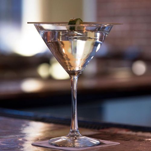 A close-up of a martini glass filled with a clear cocktail, garnished with a slice of lime.