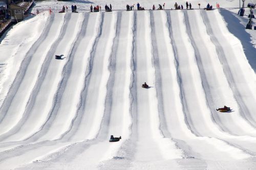 A snowy hill with multiple lanes, featuring people sledding down on inflatable tubes.