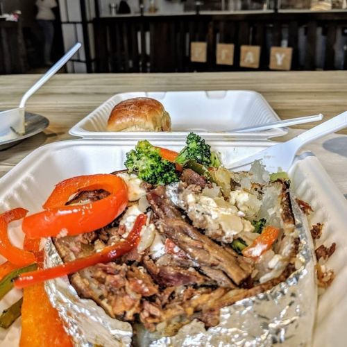 A foil-wrapped meal with beef, vegetables, and a roll on a table, with a cozy dining atmosphere in the background.