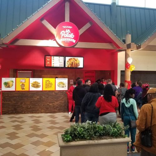 A busy food stall with a red exterior, featuring a menu and a line of customers waiting to order.