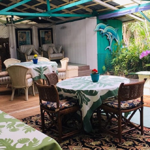 Cozy outdoor seating area with tropical decor, featuring a table with a floral tablecloth and potted plants.