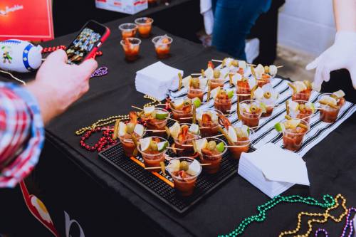 A table with small cups of garnished drinks, with a person taking a photo and colorful decorations in the background.